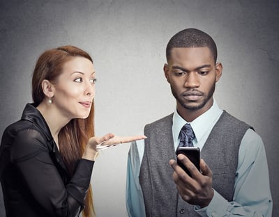 Attractive woman blowing a kiss to young handsome man who ignores her and looking at smartphone browsing internet isolated grey wall background. Phone addiction concept. Human face expression, emotion