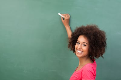 Beautiful African American student or teacher standing in front of the blank class blackboard with a piece of chalk in her hand ready to commence writing