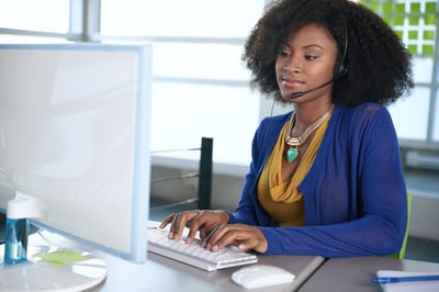 Portrait of a smiling customer service representative with an afro at the computer using headset