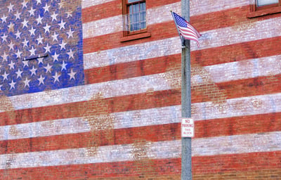 Small-town street scene in Illinois American flag flapping in breeze by huge painted American flag fading from brick wall